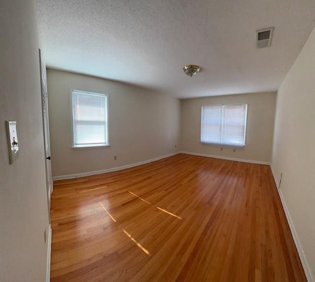 spare room with baseboards, a textured ceiling, visible vents, and light wood-style floors