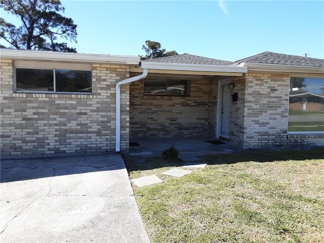 view of front of property featuring a front yard, roof with shingles, and brick siding