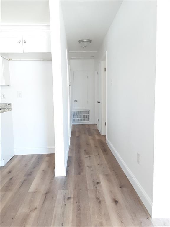 corridor with light wood-type flooring, visible vents, and baseboards