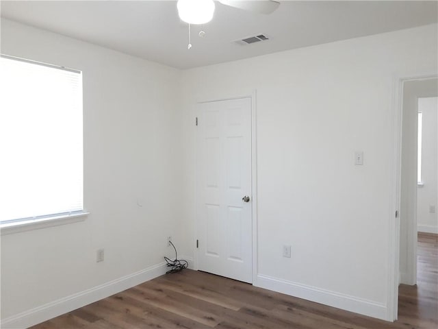 unfurnished room with a ceiling fan, wood finished floors, visible vents, and baseboards