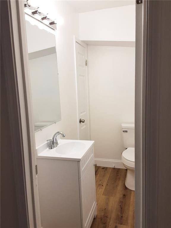 bathroom featuring toilet, baseboards, wood finished floors, and vanity