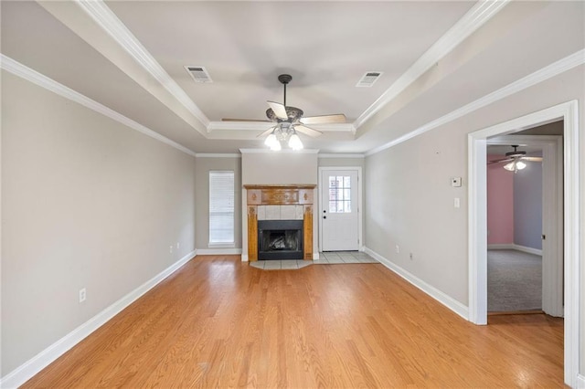 unfurnished living room featuring visible vents, baseboards, light wood-style floors, a tray ceiling, and a tiled fireplace