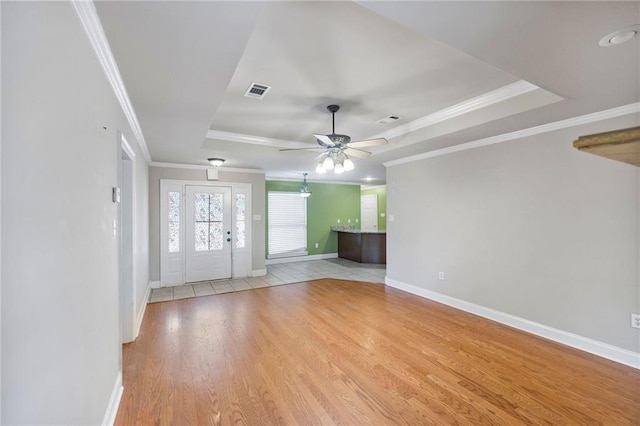 unfurnished living room with baseboards, visible vents, a tray ceiling, crown molding, and light wood-type flooring