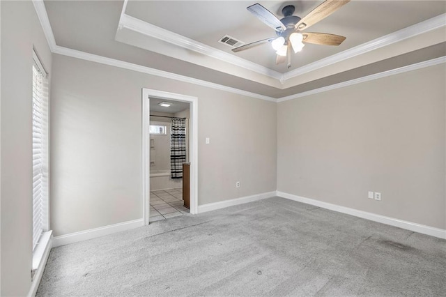 carpeted empty room featuring crown molding, a raised ceiling, visible vents, a ceiling fan, and baseboards