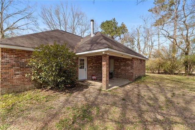 rear view of house with brick siding, a lawn, and a patio area