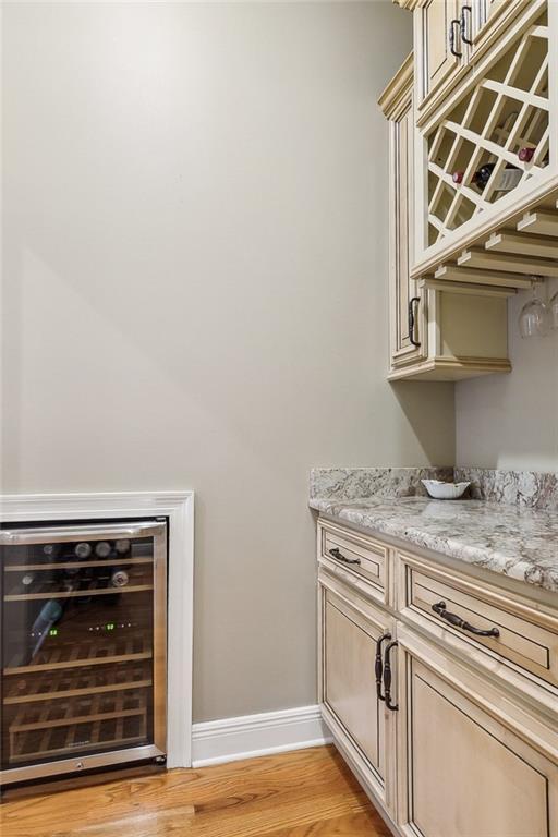 bar featuring light wood-style flooring, beverage cooler, and baseboards