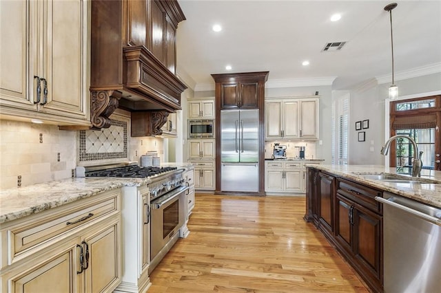 kitchen with light wood-type flooring, pendant lighting, a sink, crown molding, and built in appliances