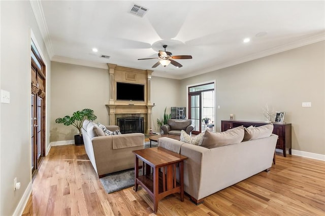 living area with baseboards, visible vents, crown molding, light wood-type flooring, and a large fireplace