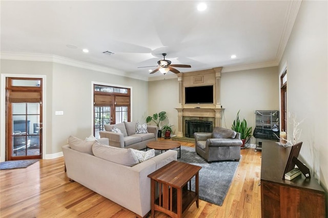 living room featuring light wood finished floors, visible vents, crown molding, ceiling fan, and a fireplace