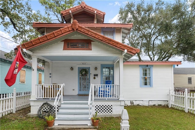 view of front facade with a front yard, covered porch, fence, and metal roof