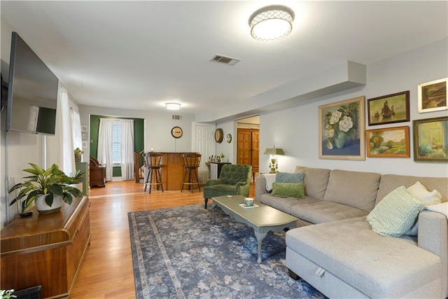 living room with light wood-style floors, visible vents, and a dry bar