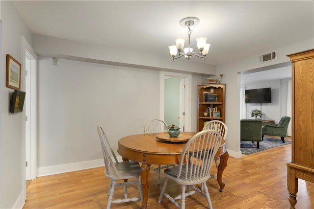 dining space with light wood finished floors, baseboards, visible vents, and a notable chandelier