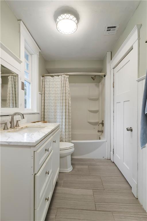 full bath featuring visible vents, toilet, vanity, and shower / tub combo with curtain