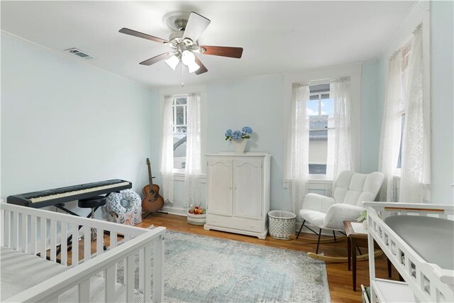 bedroom featuring visible vents, a ceiling fan, ornamental molding, wood finished floors, and a nursery area