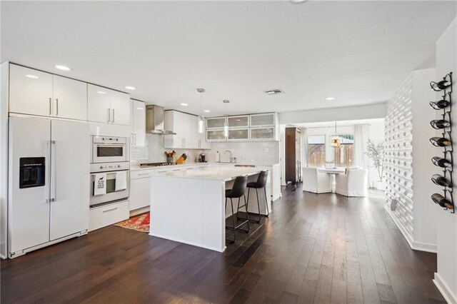 kitchen featuring dark wood-style flooring, wall chimney range hood, built in refrigerator, and a kitchen bar