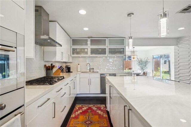 kitchen with a sink, white cabinets, light countertops, appliances with stainless steel finishes, and wall chimney exhaust hood