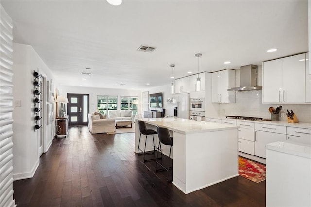 kitchen with a breakfast bar, dark wood-style flooring, white cabinets, open floor plan, and wall chimney exhaust hood