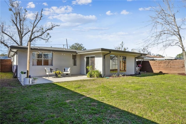 rear view of house with stucco siding, a yard, fence, and a patio