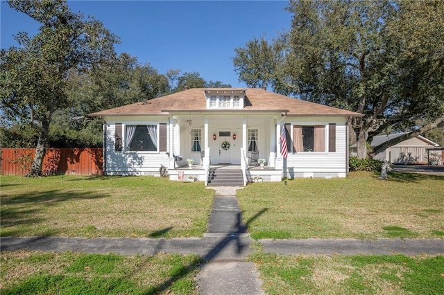 bungalow with covered porch, fence, and a front lawn