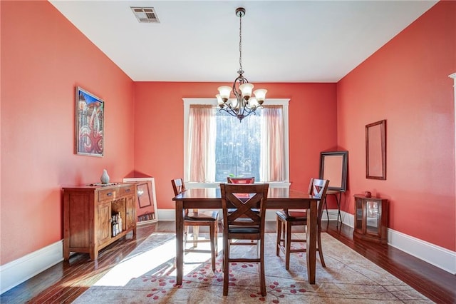 dining room with a notable chandelier, baseboards, visible vents, and wood finished floors