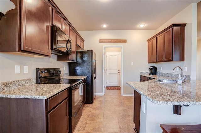 kitchen featuring a sink, black appliances, light stone countertops, a peninsula, and a kitchen breakfast bar