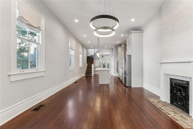 unfurnished living room with dark wood-style floors, a premium fireplace, visible vents, and stairway