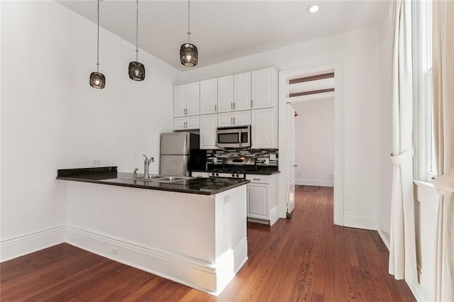 kitchen with stainless steel appliances, dark countertops, tasteful backsplash, a sink, and a peninsula