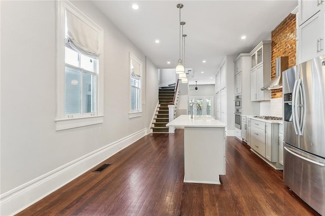 kitchen featuring a center island with sink, baseboards, dark wood-style flooring, stainless steel appliances, and light countertops