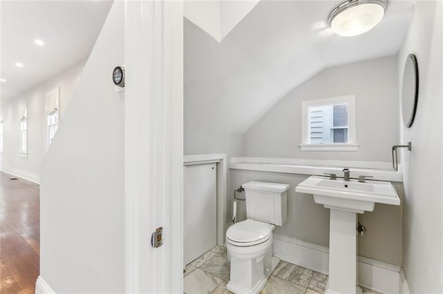 half bath with a healthy amount of sunlight, baseboards, toilet, and lofted ceiling