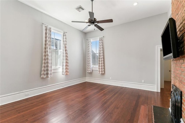 unfurnished living room featuring wood finished floors, a ceiling fan, visible vents, baseboards, and a brick fireplace