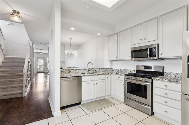 kitchen featuring stainless steel appliances, white cabinetry, a sink, and light stone countertops