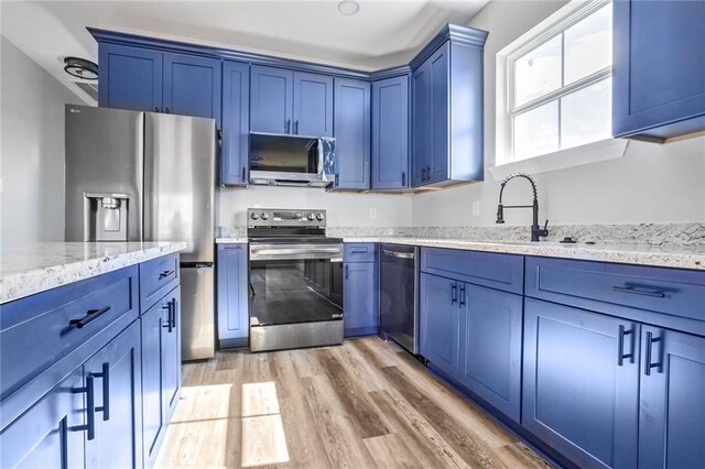 7909 Tarpon St, New Orleans, LA 70126 - kitchen featuring stainless steel appliances, blue cabinetry, light wood-style flooring, and light stone counters