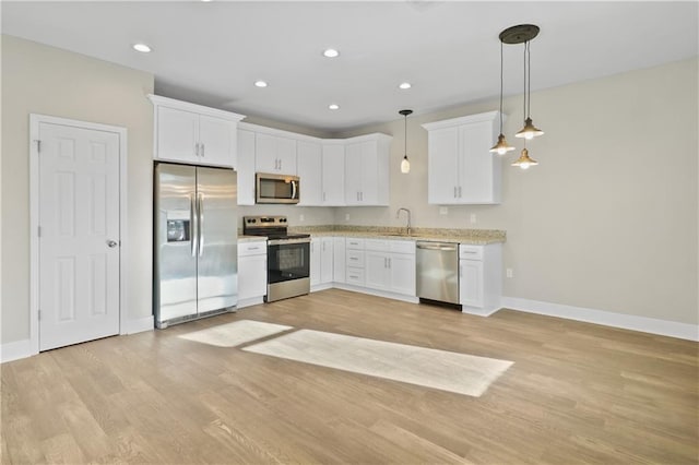 kitchen featuring light wood finished floors, a sink, baseboards, white cabinets, and appliances with stainless steel finishes