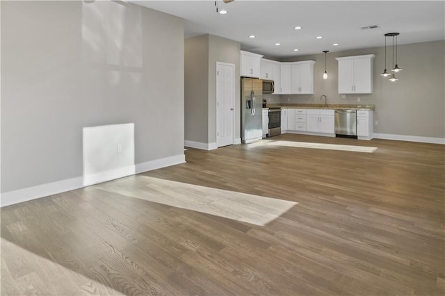 unfurnished living room with recessed lighting, light wood finished floors, a sink, baseboards, and visible vents