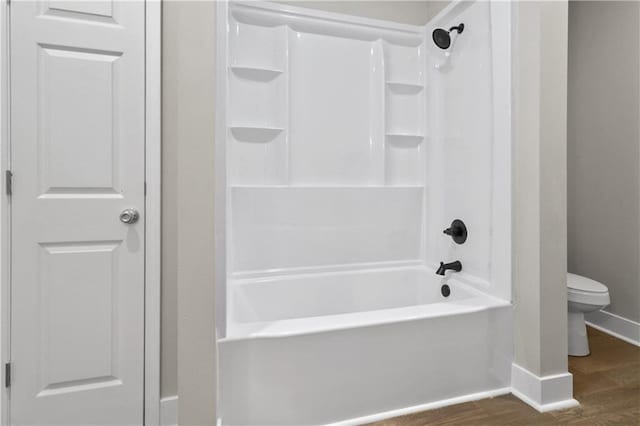 bathroom with baseboards, wood finished floors, toilet, and shower / washtub combination