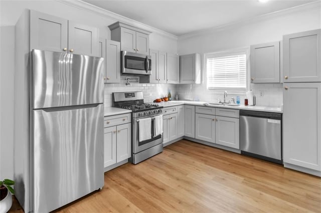 kitchen with stainless steel appliances, ornamental molding, a sink, and light countertops