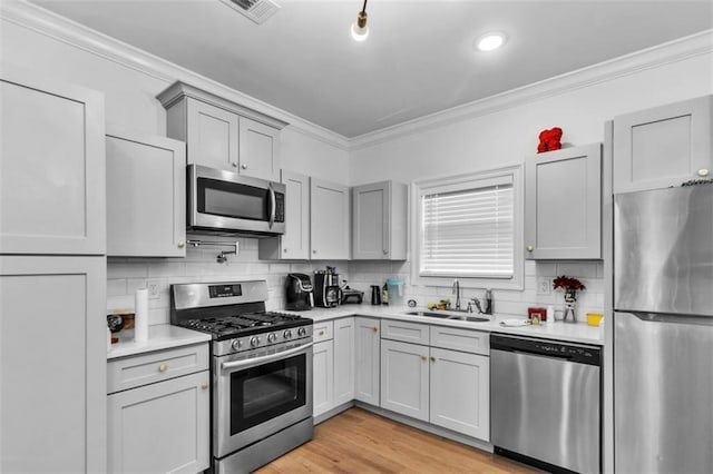 kitchen with ornamental molding, light countertops, appliances with stainless steel finishes, and a sink