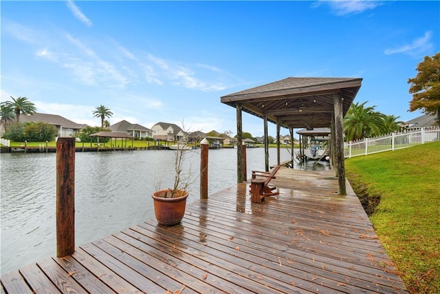 view of dock with a water view, a residential view, fence, and a lawn