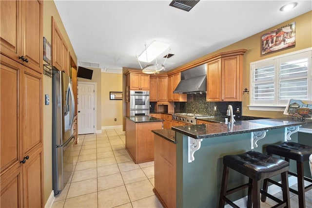 kitchen with stainless steel appliances, a peninsula, a center island, brown cabinets, and wall chimney exhaust hood