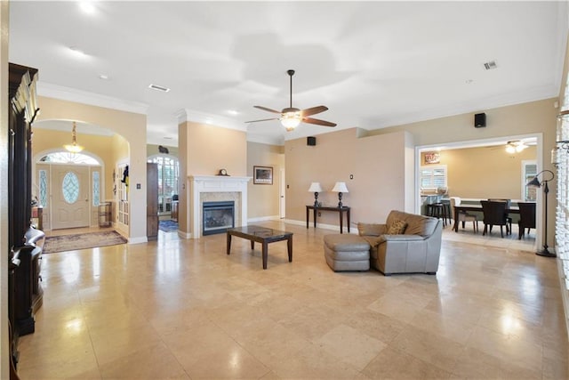 living area featuring arched walkways, a fireplace, visible vents, baseboards, and ornamental molding