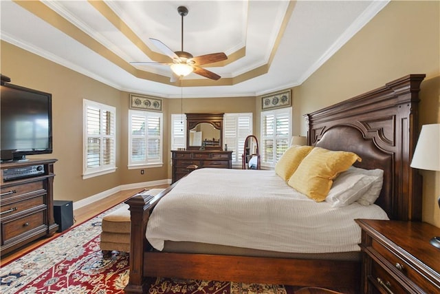 bedroom featuring baseboards, a raised ceiling, ceiling fan, ornamental molding, and wood finished floors