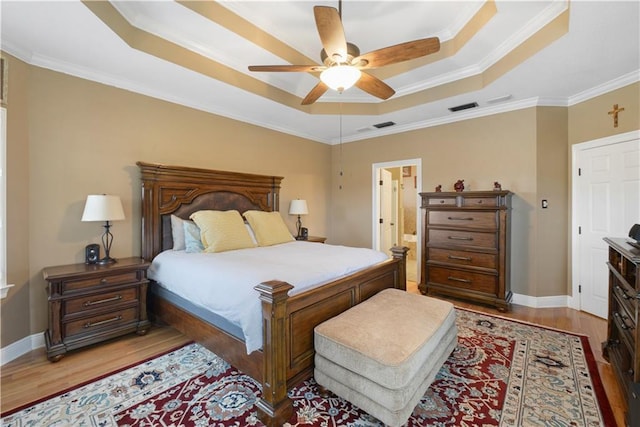 bedroom featuring light wood-style flooring, a raised ceiling, visible vents, and baseboards