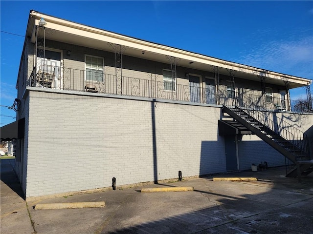 back of house featuring stairs, uncovered parking, and brick siding