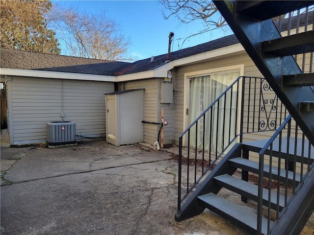 rear view of property with a patio, central AC unit, and roof with shingles