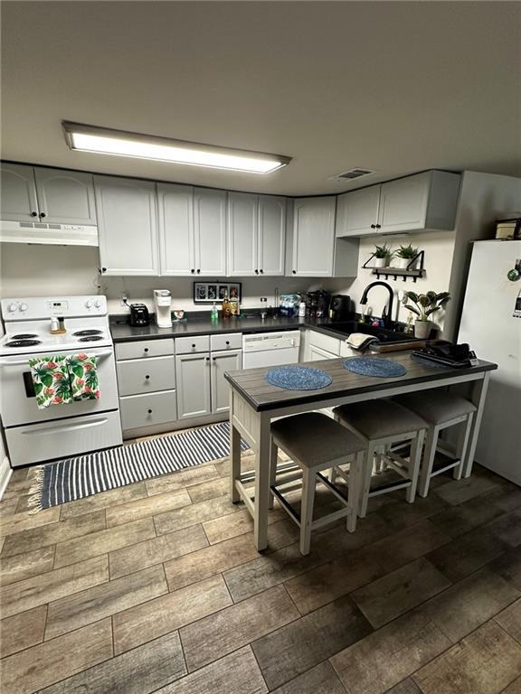 kitchen featuring white appliances, visible vents, a sink, under cabinet range hood, and dark countertops