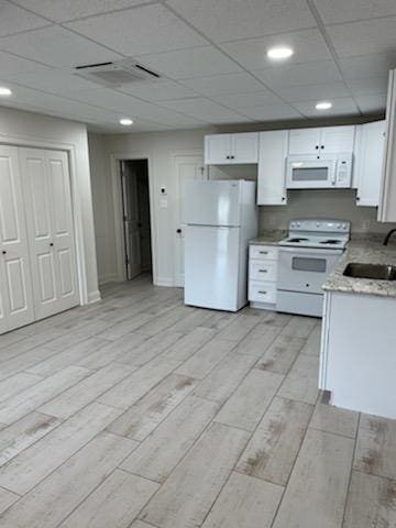 kitchen with visible vents, wood finish floors, white cabinets, white appliances, and a sink