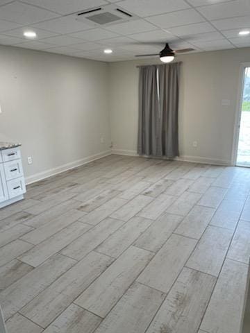 spare room featuring light wood finished floors, a paneled ceiling, and baseboards