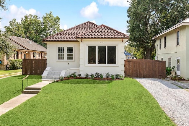 view of front facade with a front yard, a tile roof, fence, and stucco siding