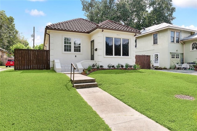 mediterranean / spanish-style home with a front yard, a tile roof, fence, and stucco siding