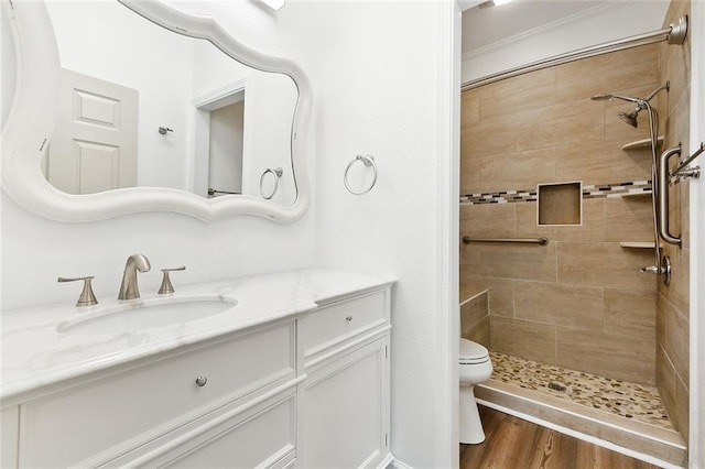 bathroom featuring toilet, a tile shower, wood finished floors, and vanity